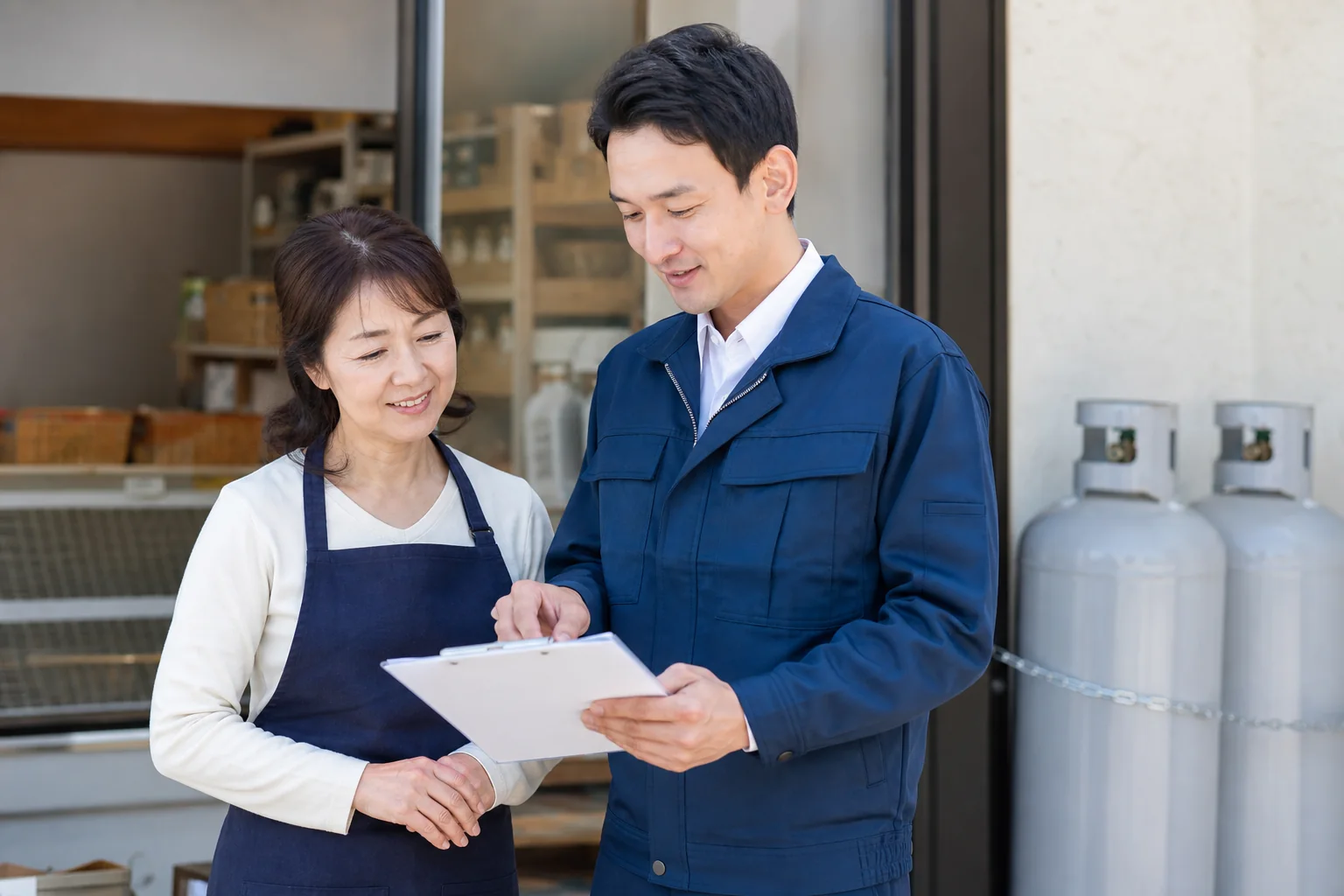 ガスボンベ回収前に見積書を確認する店舗のお客様とスタッフ